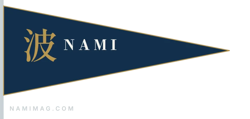 The Nami burgee: a navy pennant edged in brass with 波 NAMI, on a white staff, namimag.com below.