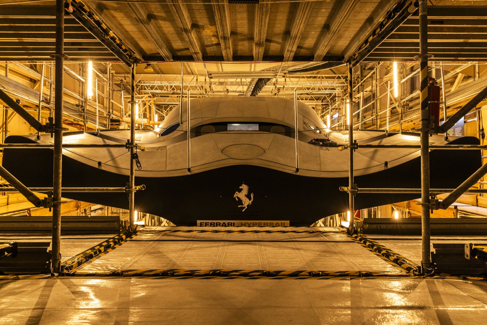 The hull of Ferrari Hypersail inside the shipyard scaffolding, with the Prancing Horse and the name on its plate.